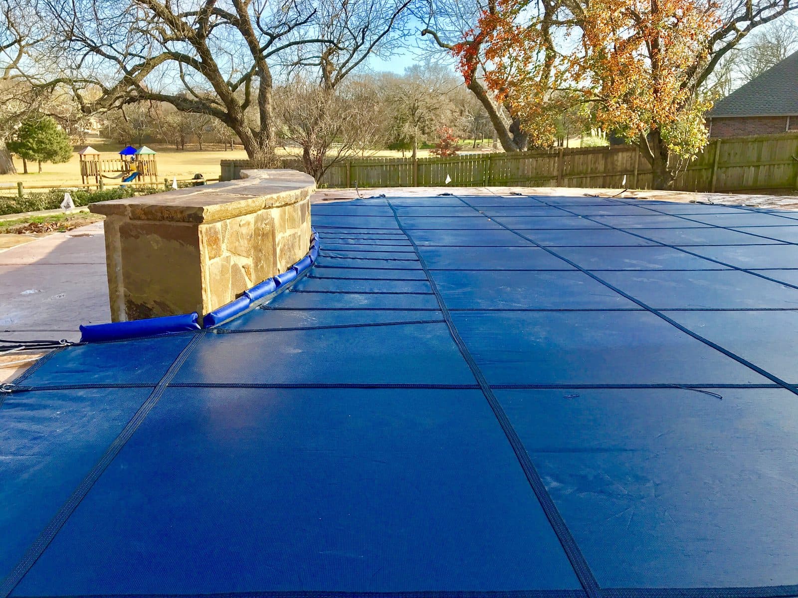 Blue inground pool safety cover anchored along a raised stone wall