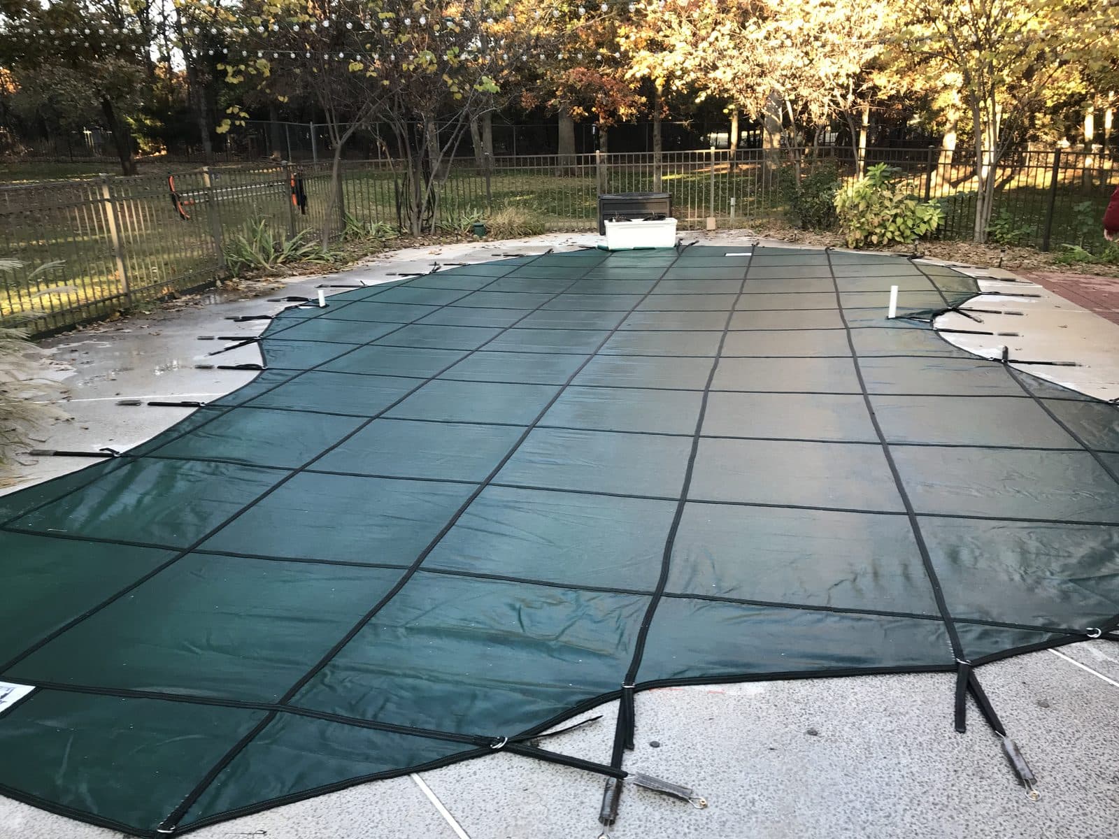 Green safety cover on a freeform inground pool with an aluminum fence