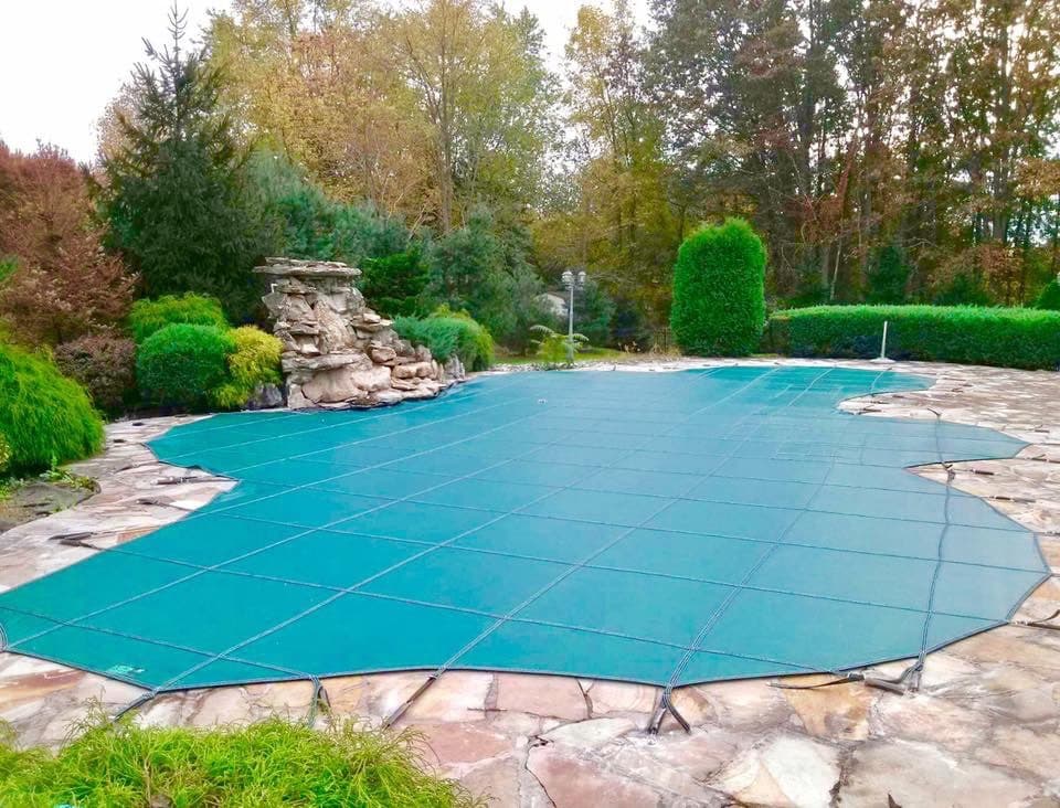Green safety cover on a freeform inground pool with a stone waterfall