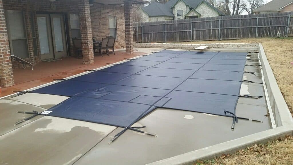 Navy safety cover closed over an inground pool for winter behind a brick ranch home